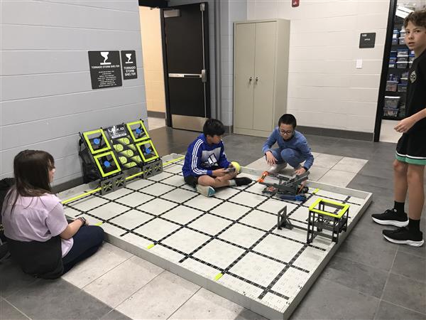 Students test robots on VEX IQ competition field at practice.